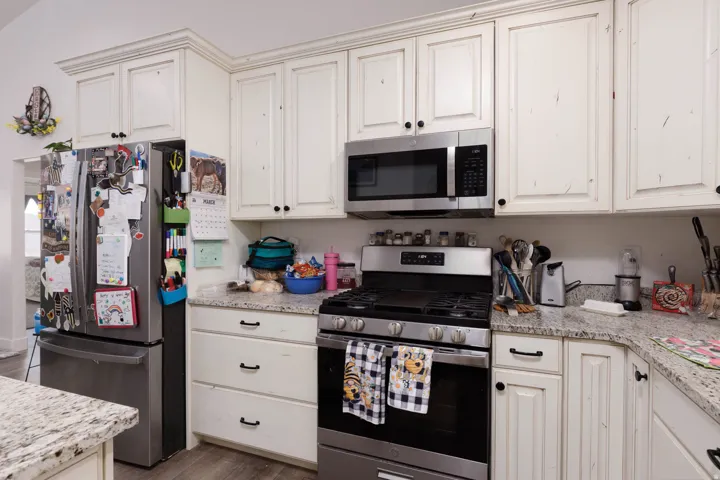 Kitchen with stainless steel appliances, light stone countertops, wood finished floors, white cabinetry, and cream cabinets