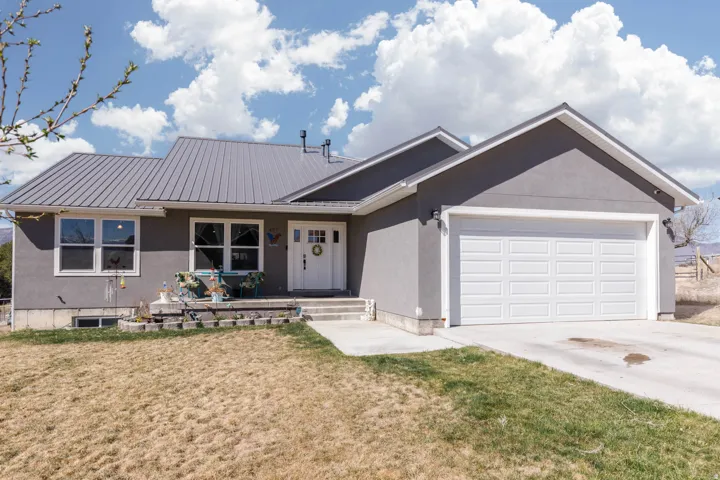 Single story home featuring a garage, a front lawn, a metal roof, concrete driveway, and stucco siding