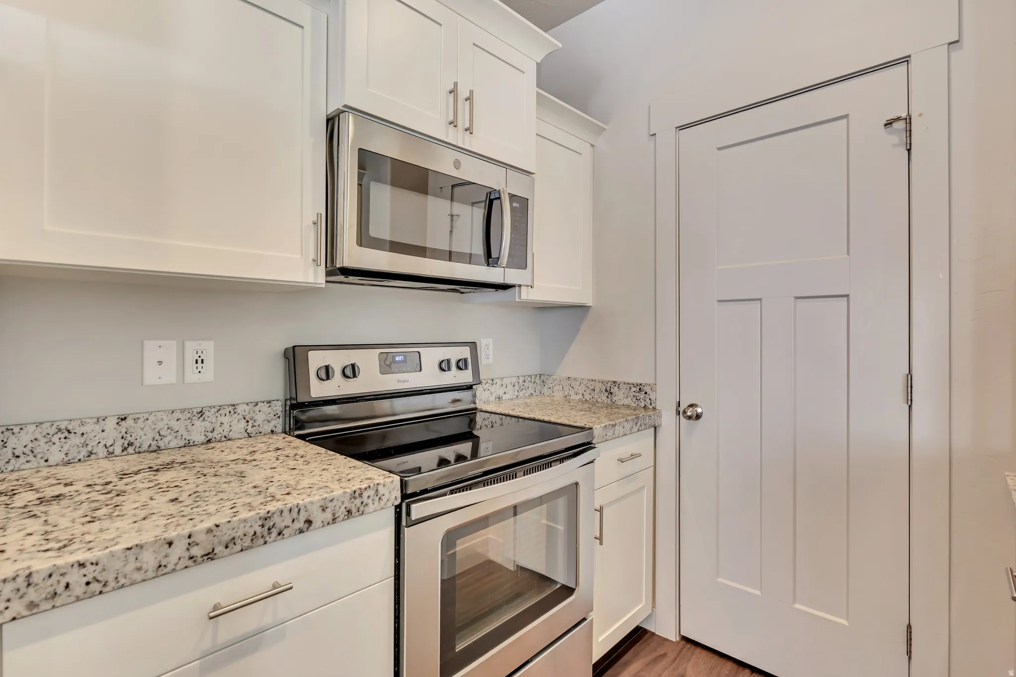 Kitchen with stainless steel appliances, white cabinets, light stone countertops, and light wood finished floors