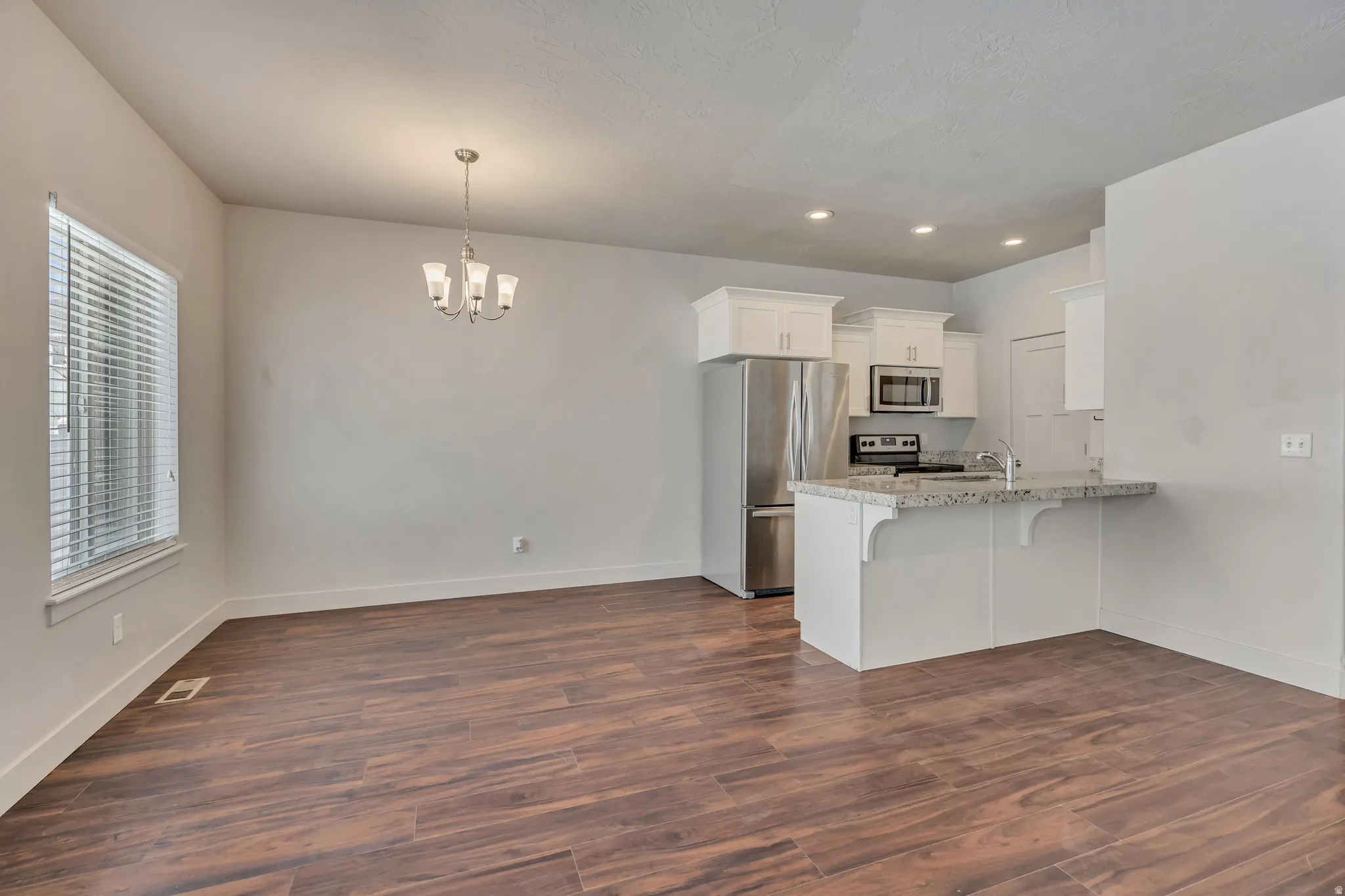 Kitchen with a kitchen bar, stainless steel appliances, dark wood-style flooring, white cabinets, and a peninsula