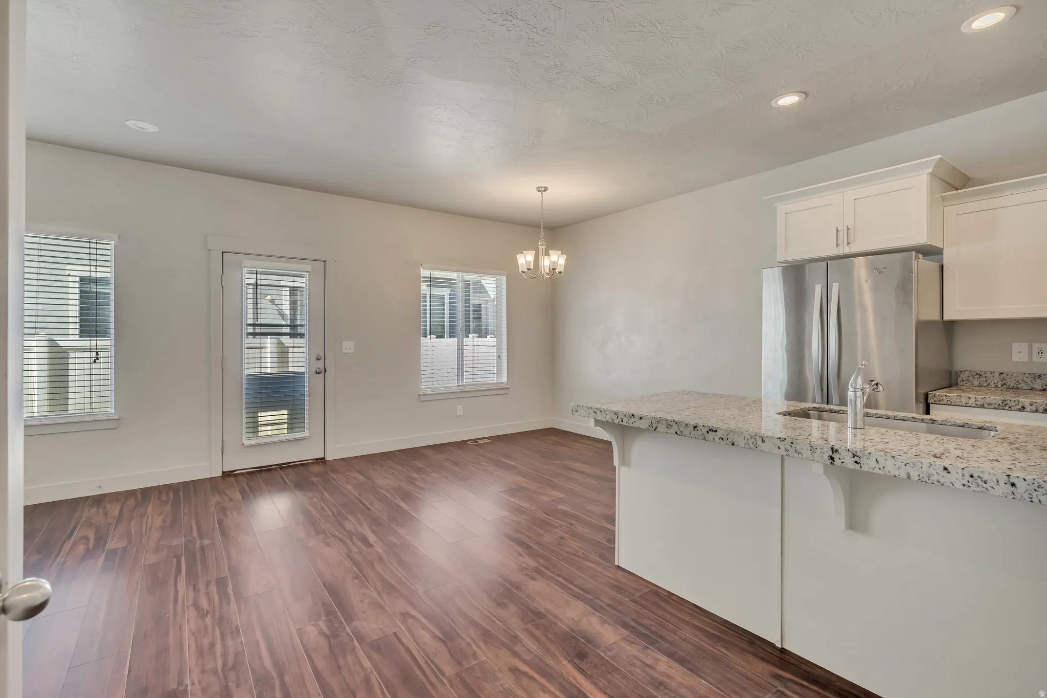 Kitchen with white cabinetry, light stone counters, freestanding refrigerator, dark wood-type flooring, and suspended lighting