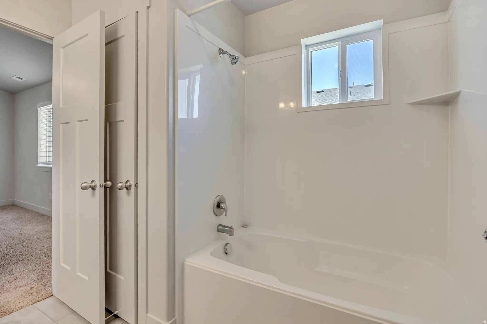 Bathroom with bathtub / shower combination, healthy amount of natural light, light carpet, and light tile patterned floors