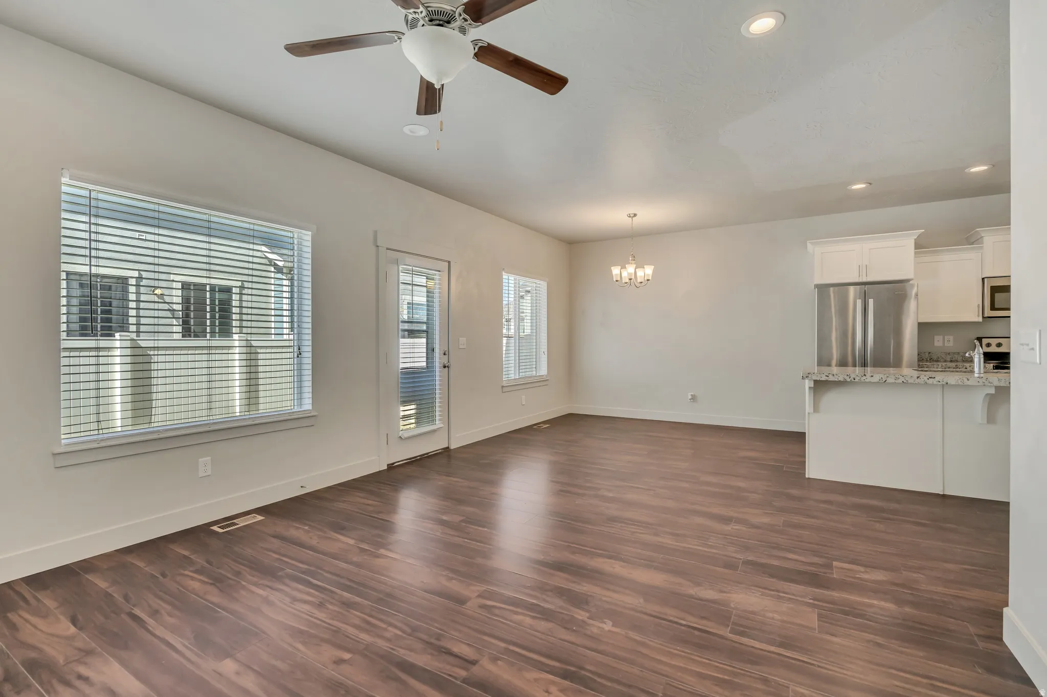 Unfurnished living room with ceiling fan, dark wood-style floors, and a chandelier