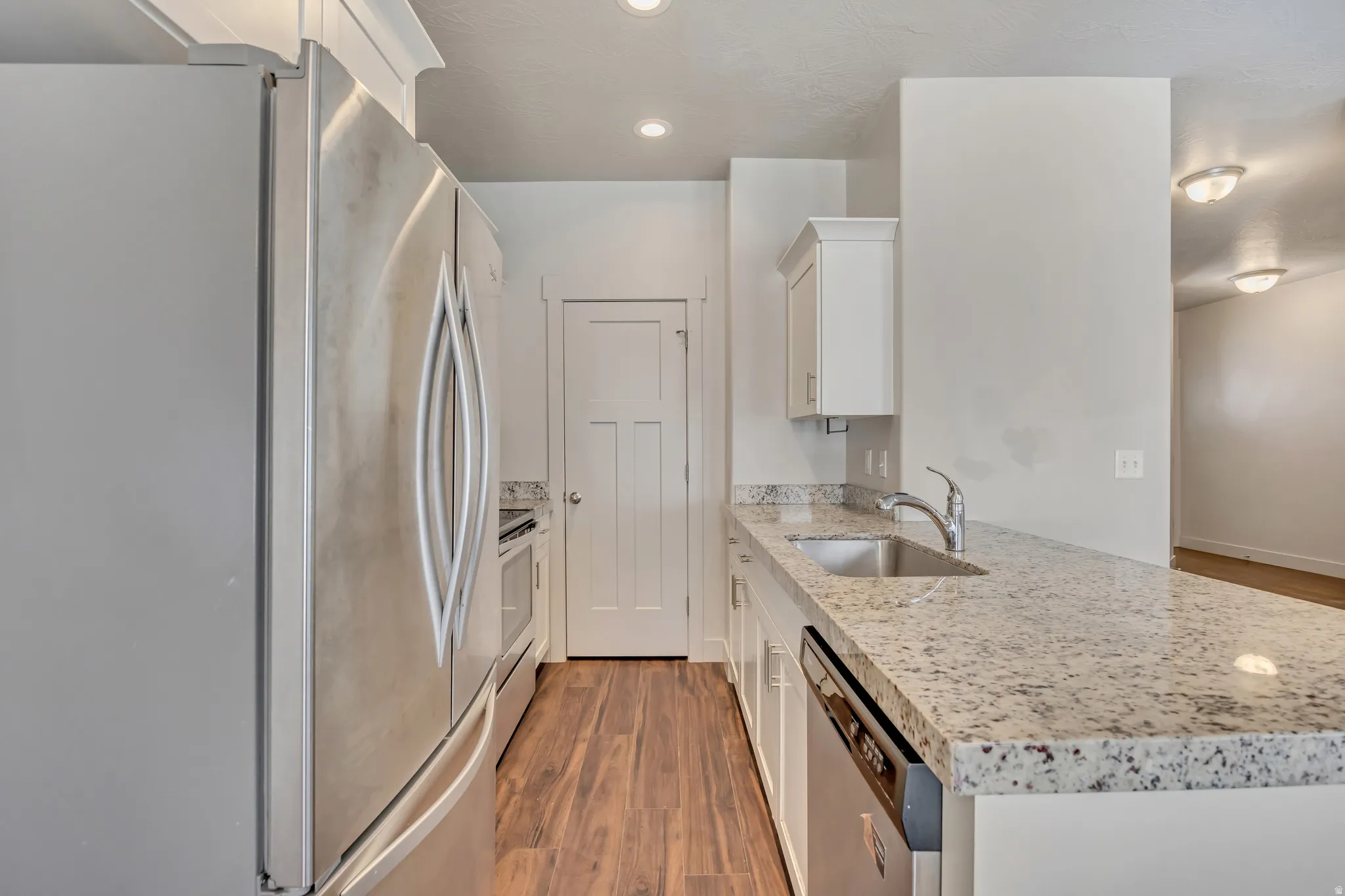 Kitchen with stainless steel appliances, light stone counters, dark wood-style flooring, white cabinetry, and recessed lighting