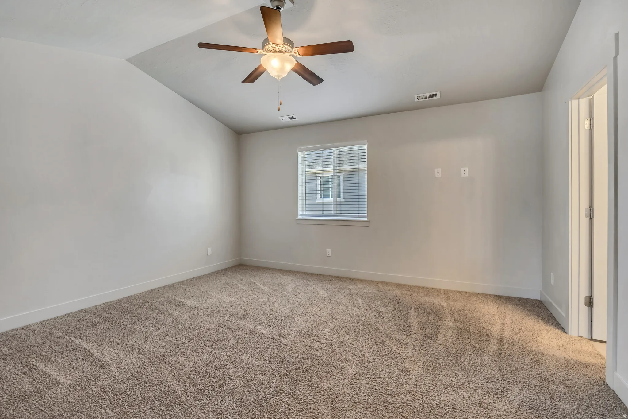Empty room with light colored carpet, lofted ceiling, and ceiling fan