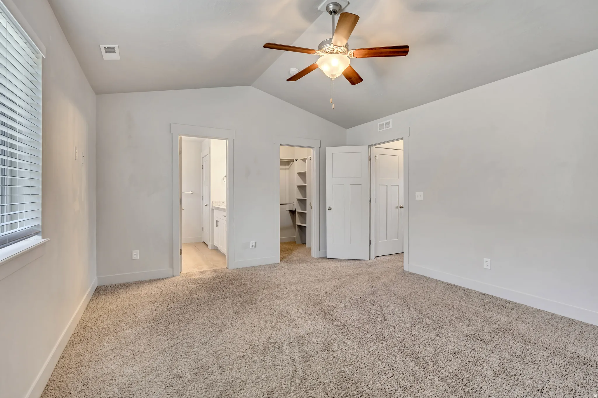 Unfurnished bedroom featuring light colored carpet, a spacious closet, a ceiling fan, and ensuite bathroom