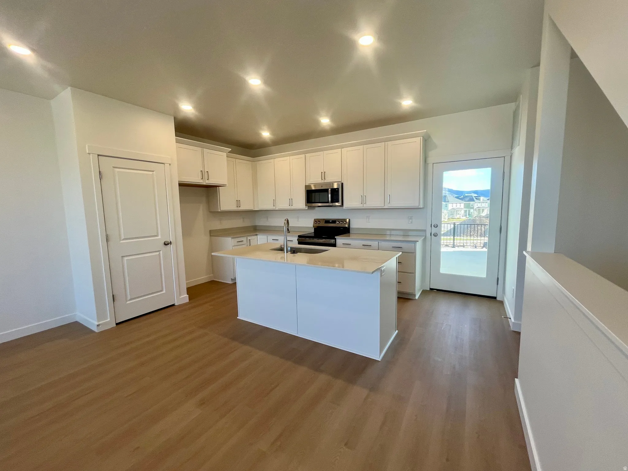 Kitchen featuring white cabinetry, dark wood-type flooring, stainless steel appliances, recessed lighting, and a center island with sink