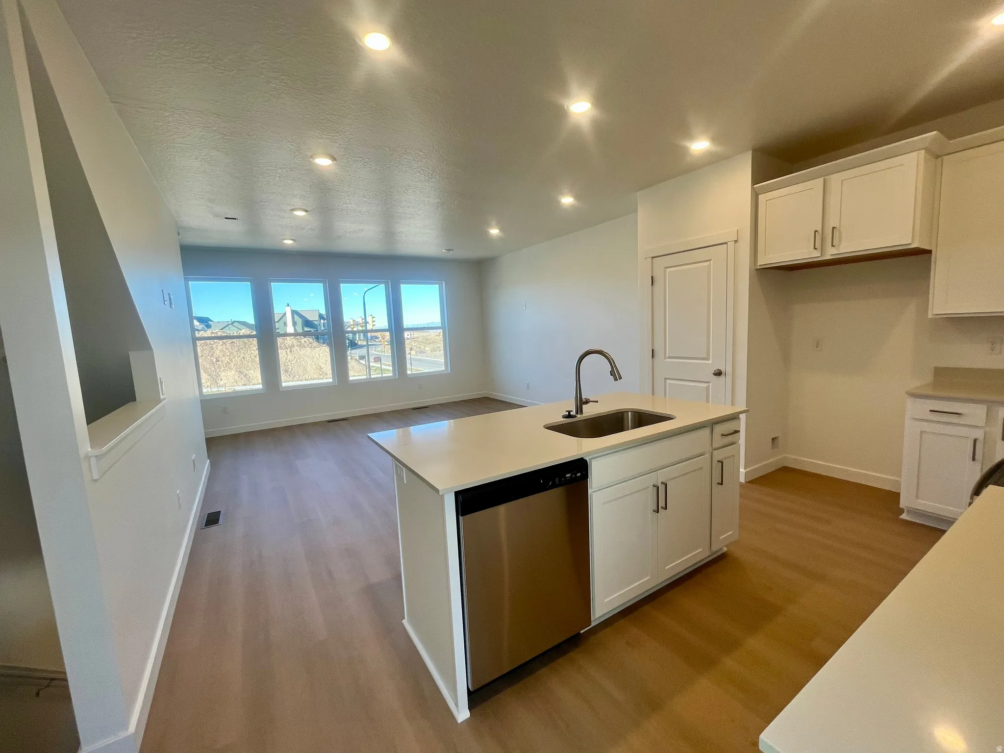 Kitchen with white cabinetry, a center island with sink, light wood finished floors, dishwasher, and recessed lighting