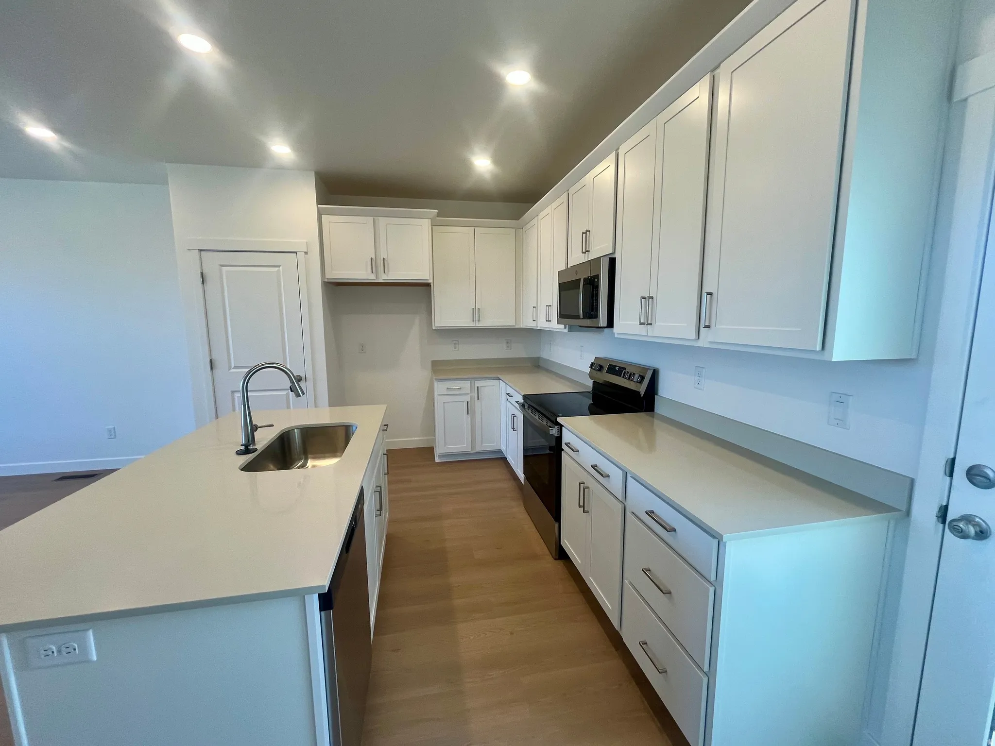 Kitchen with stainless steel appliances, white cabinets, a center island with sink, dark wood finished floors, and recessed lighting
