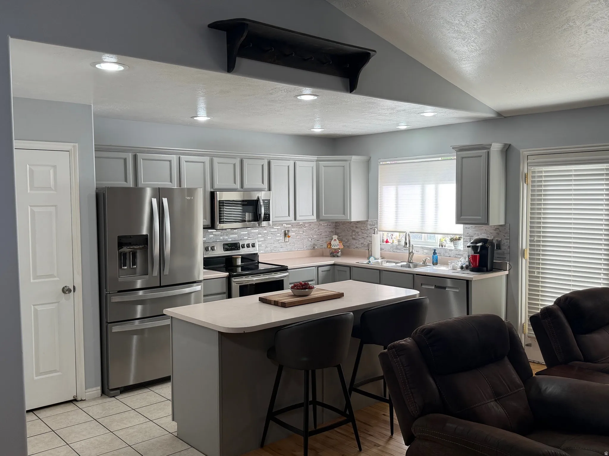 Kitchen with a kitchen bar, stainless steel appliances, gray cabinetry, light countertops, and a kitchen island