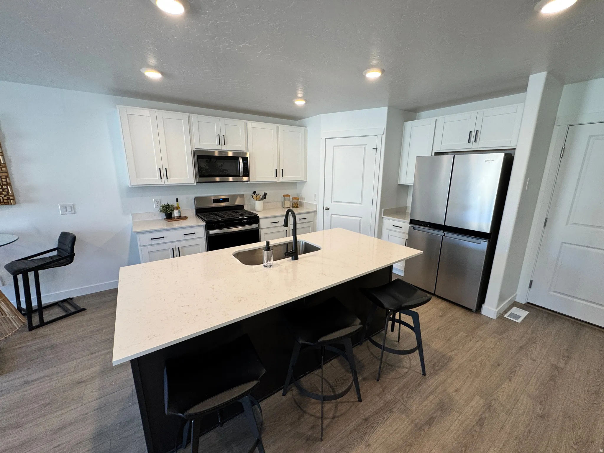 Modern kitchen featuring white shaker cabinetry, stainless steel appliances, and a central island with a light-colored countertop