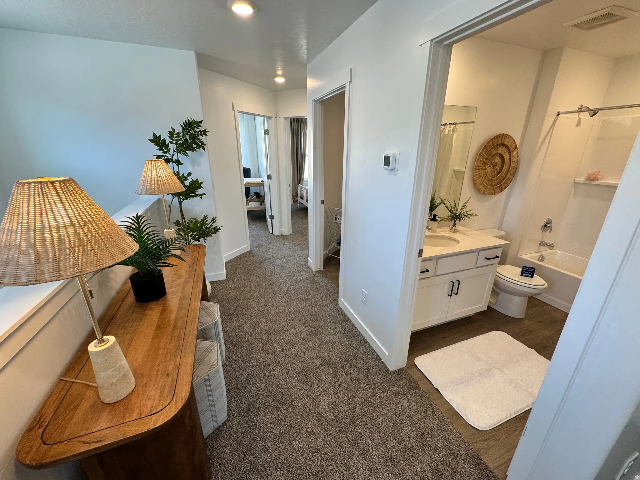 Hallway bath with a white vanity, integrated sink, and dark hardware, alongside a standard tub and shower combination