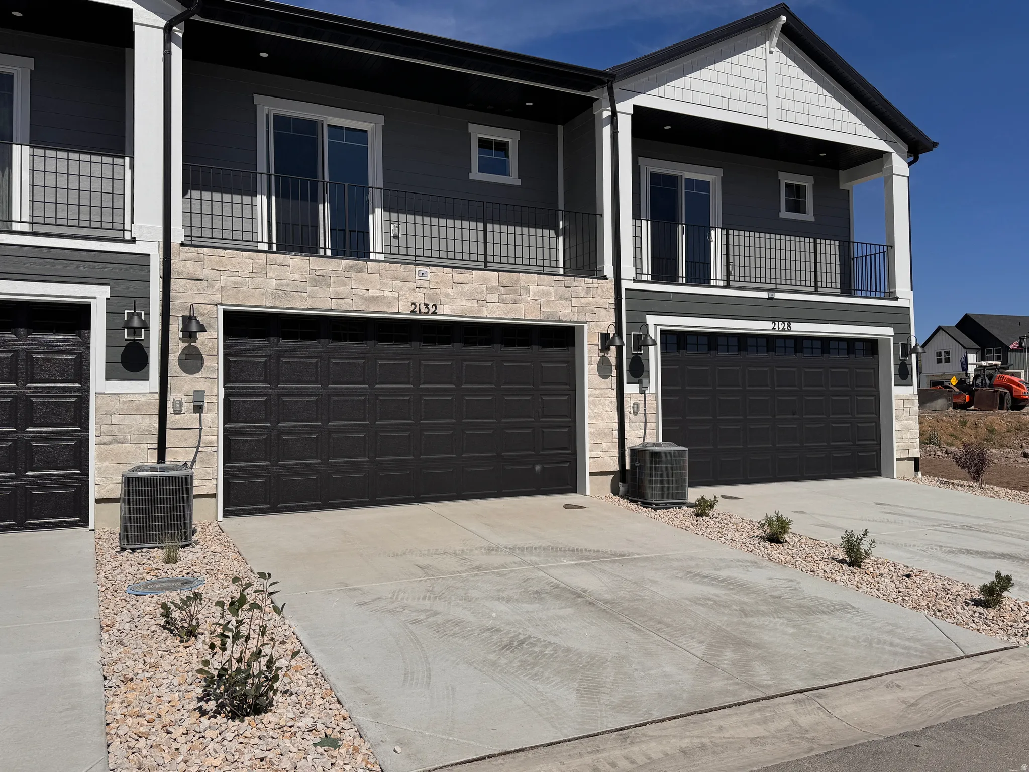 Contemporary townhome exterior featuring dark gray siding, stone veneer accents, and a prominent front-facing garage with a black door
