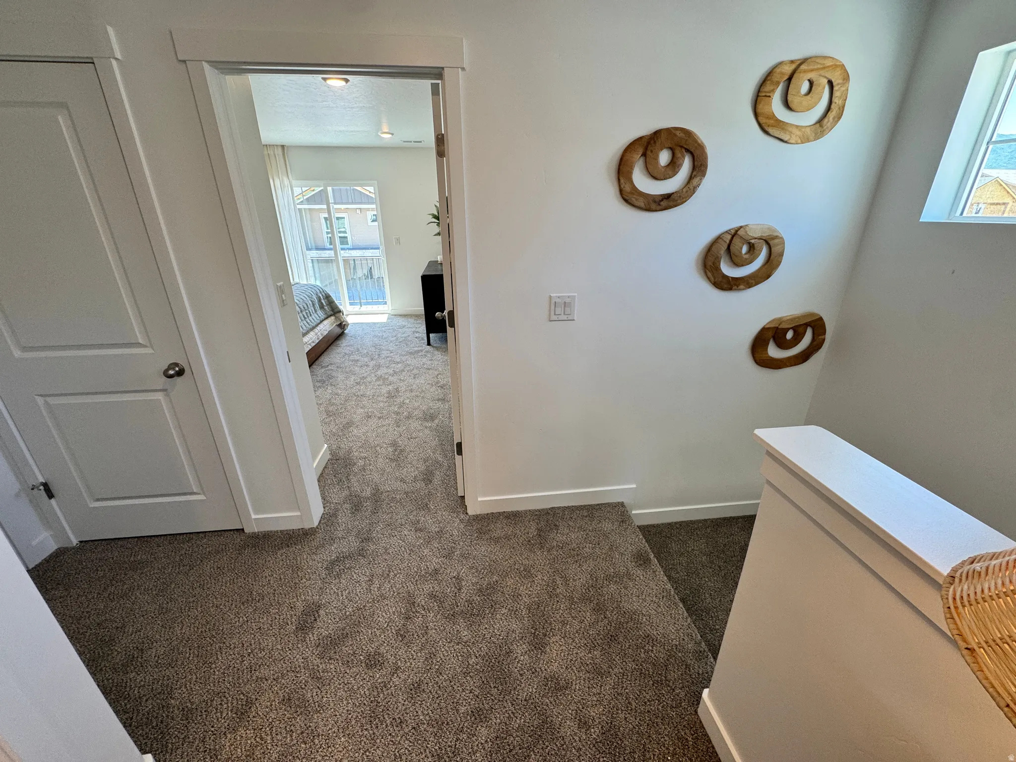 Carpeted hallway with white trim and a white door leading to an additional carpeted room with a sliding glass door