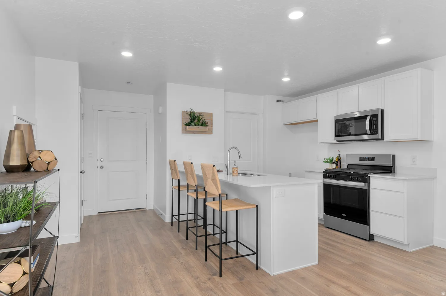 Kitchen featuring stainless steel appliances, a breakfast bar area, white cabinetry, light wood-type flooring, and recessed lighting