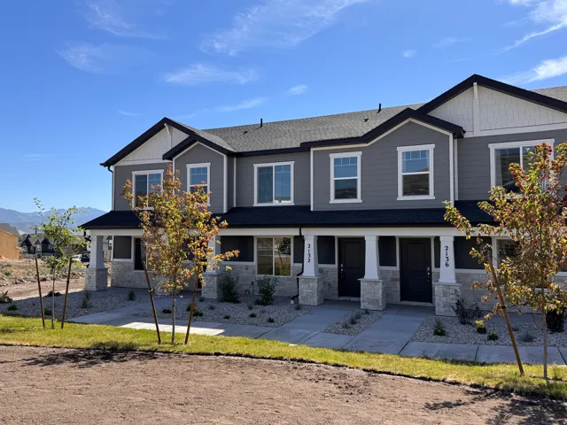 Modern townhome exterior featuring gray siding, white trim, stone accents, and a dark shingle roof