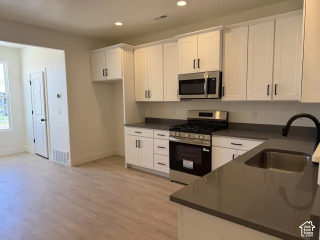 Modern kitchen featuring white shaker cabinetry, stainless steel appliances, dark countertops, a stainless steel sink with a matte black faucet, and wood-finish flooring