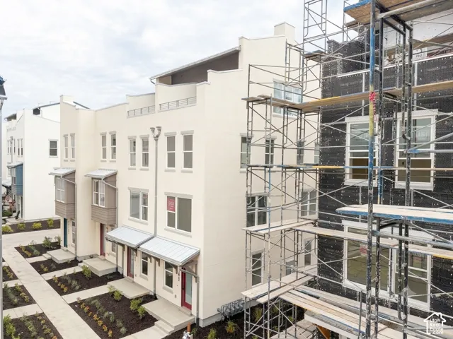 Cream-colored multi-story townhomes with white trim windows, metal awnings, and red entry doors
