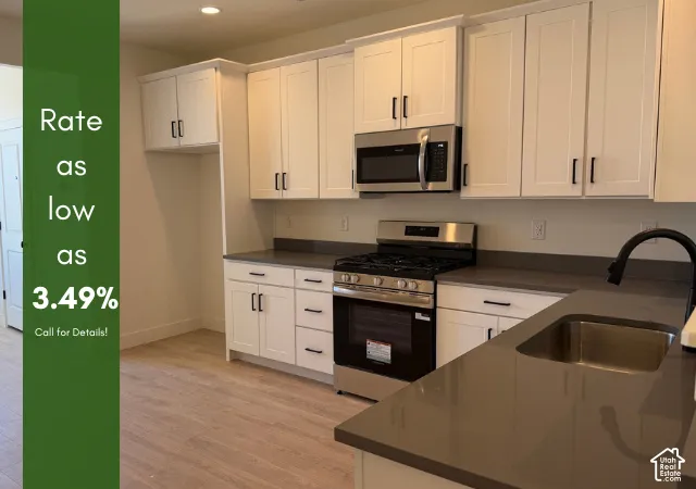 White shaker cabinetry, stainless steel appliances, dark countertops, wood-finish flooring, and a stainless steel sink with a matte black faucet