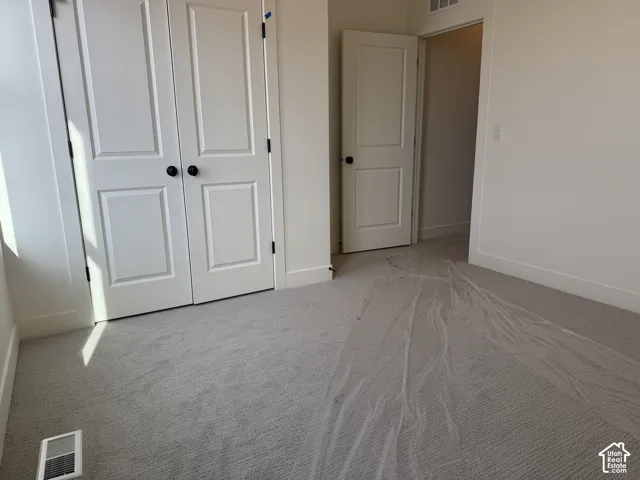 Unfurnished bedroom with light carpet and a closet