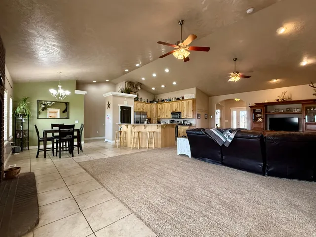 Living area featuring arched walkways, light tile patterned flooring, light carpet, vaulted ceiling, and ceiling fan
