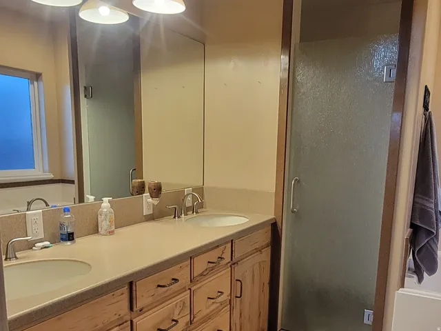 Full bath with double vanity, light tile patterned flooring, and a stall shower