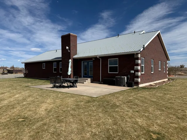 Rear view of house with a patio, a metal roof, a chimney, a lawn, and brick siding