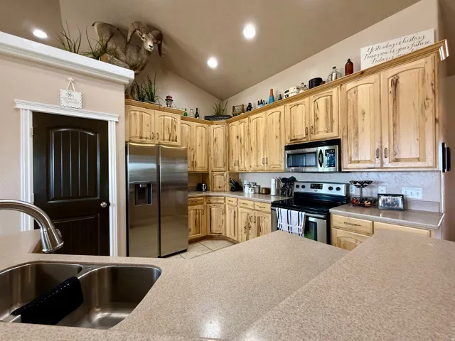 Kitchen with lofted ceiling, stainless steel appliances, light countertops, light wood finish cabinetry, and recessed lighting