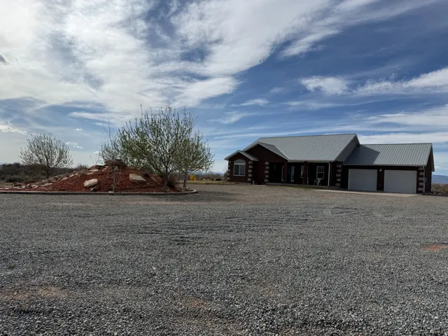 View of front facade with gravel driveway, a garage, log siding, and a metal roof
