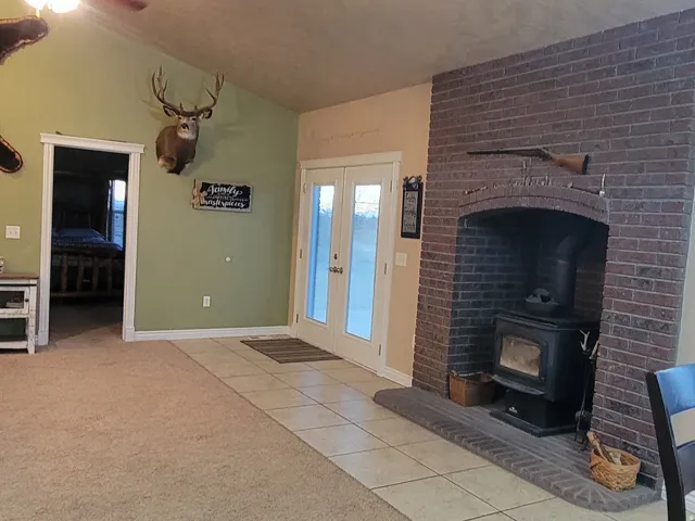 Unfurnished living room with light tile patterned flooring, a wood stove, a ceiling fan, light colored carpet, and french doors