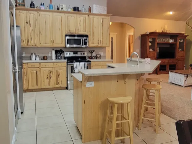 Kitchen with a breakfast bar, stainless steel appliances, light tile patterned floors, open floor plan, and light wood finish cabinets