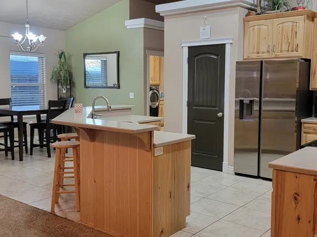 Kitchen featuring light tile patterned flooring, stainless steel refrigerator with ice dispenser, a breakfast bar area, a kitchen island with sink, and light countertops
