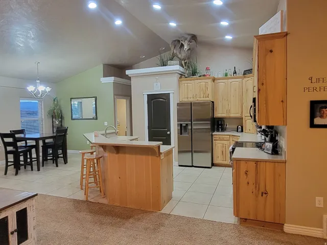 Kitchen featuring a center island with sink, light countertops, a kitchen bar, stainless steel refrigerator with ice dispenser, and light wood finish cabinets