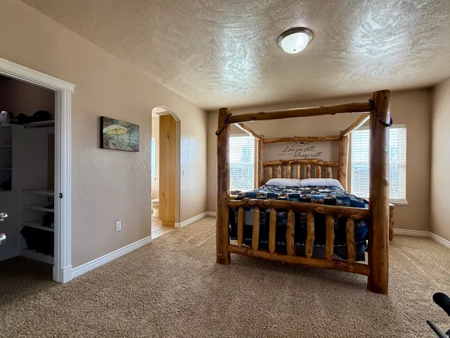Bedroom with arched walkways, light colored carpet, a textured ceiling, and a walk in closet