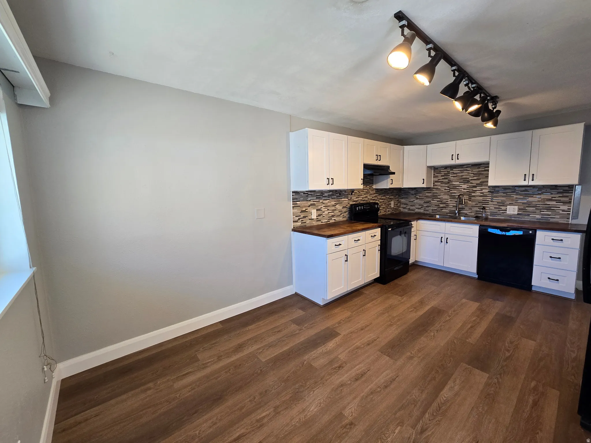 Kitchen featuring black appliances, white cabinetry, decorative backsplash, wood counters, and dark wood-style flooring