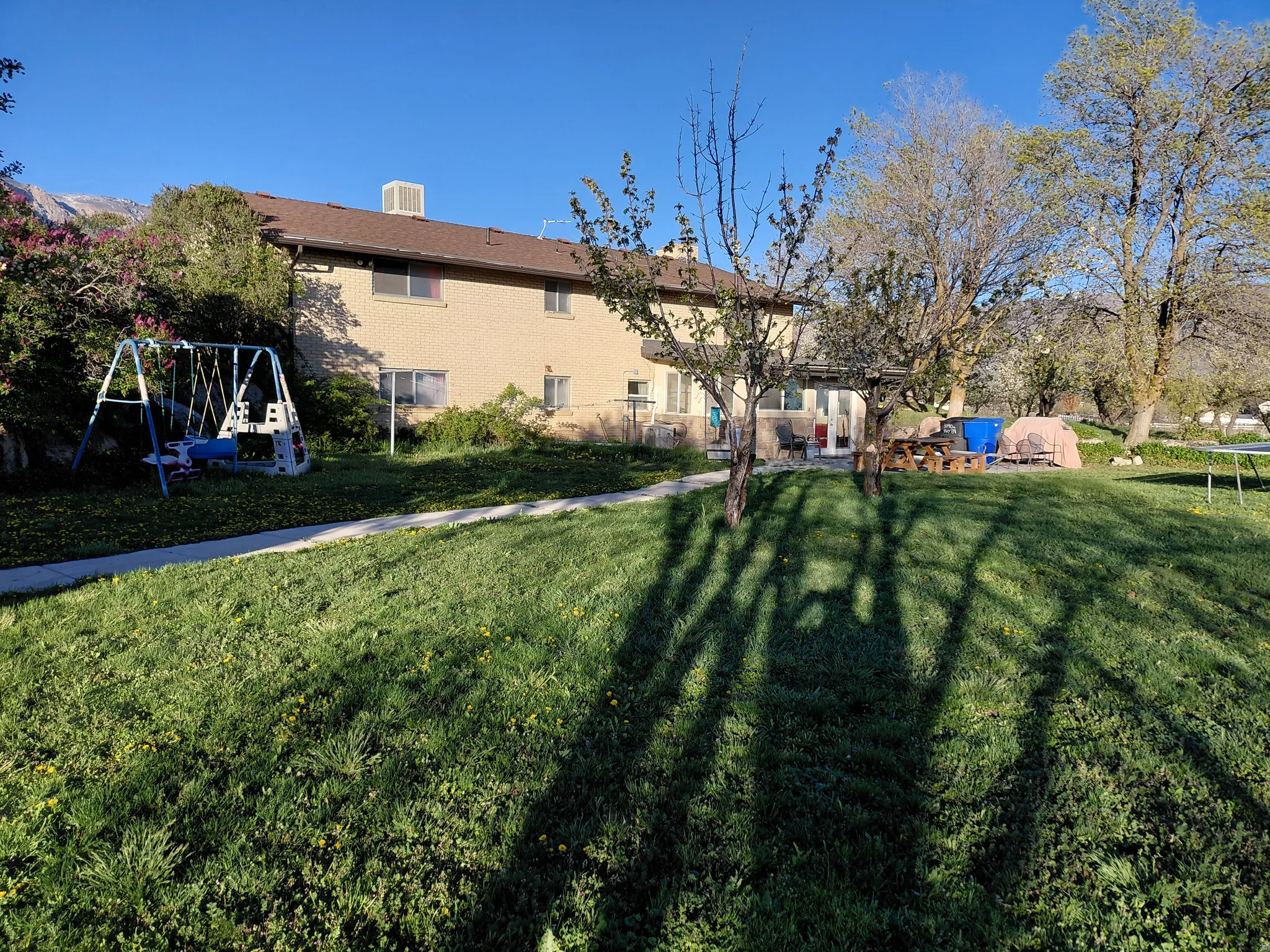Back of property featuring a trampoline, a chimney, a yard, and brick siding
