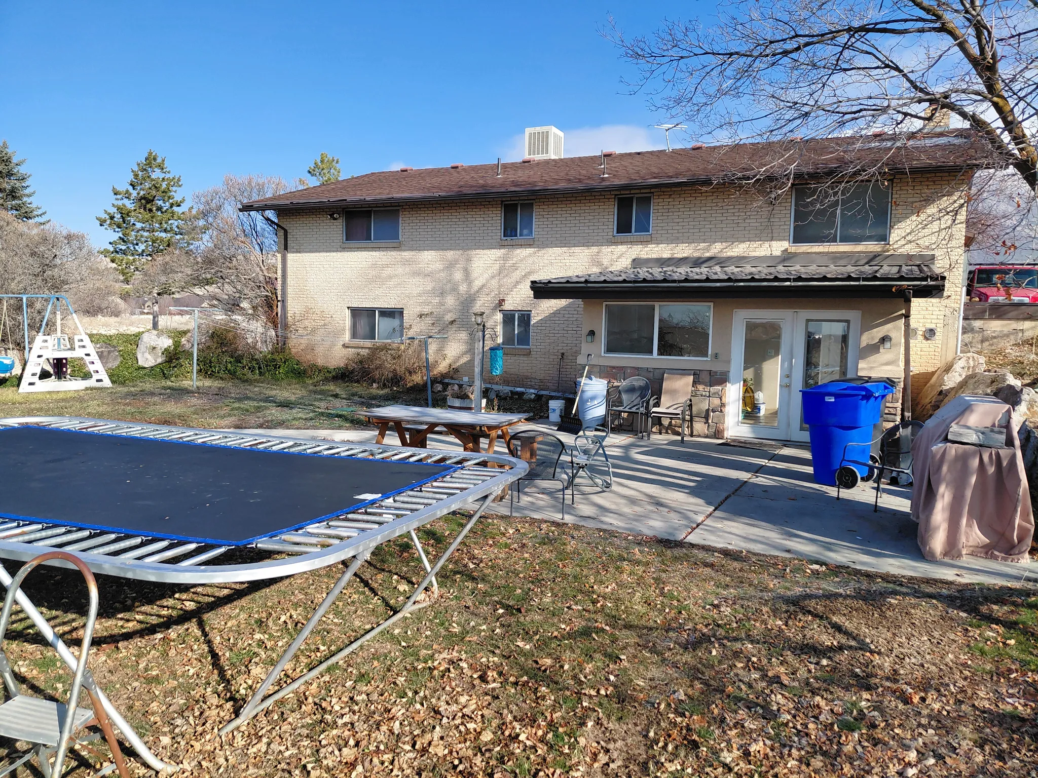 Back of property featuring a trampoline, french doors, brick siding, and a patio