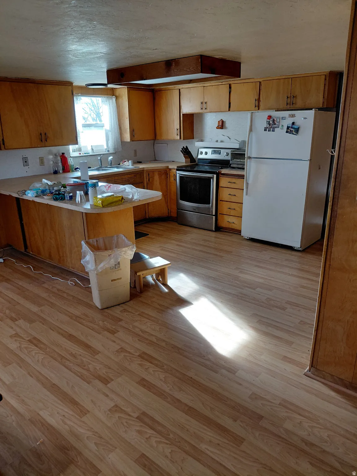 Kitchen with a peninsula, freestanding refrigerator, light countertops, stainless steel electric range oven, and light wood finished floors
