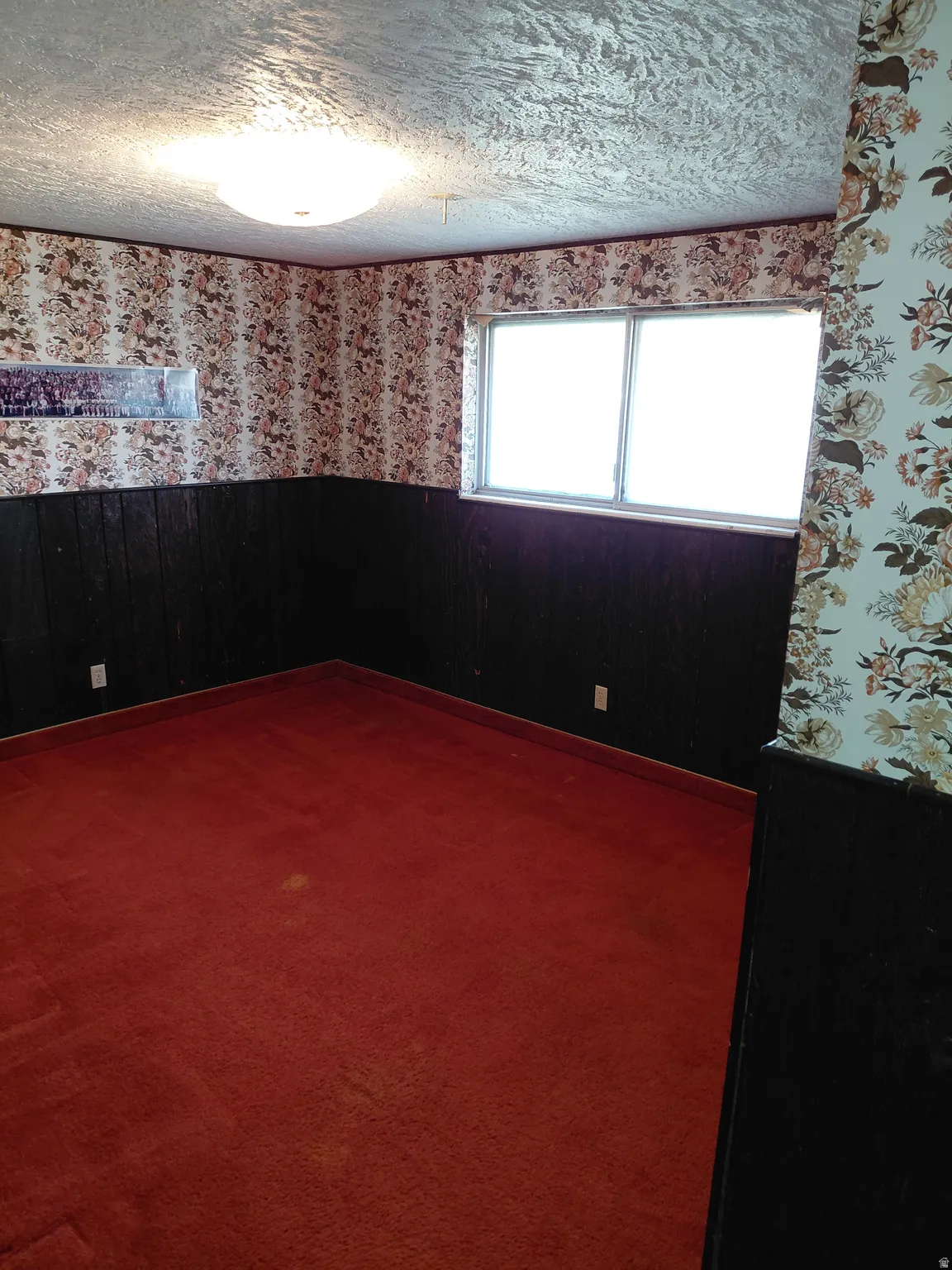 Bedroom featuring wainscoting, dark colored carpet, wallpapered walls, a textured ceiling, and wooden walls