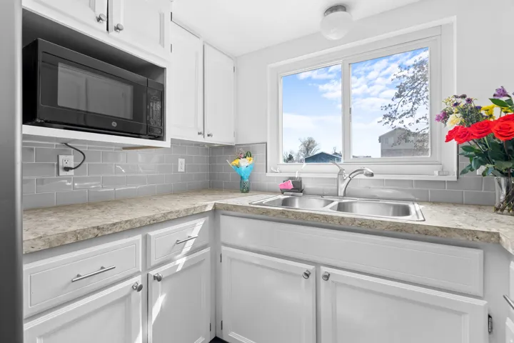 Kitchen featuring white cabinets, black microwave, light countertops, and tasteful backsplash