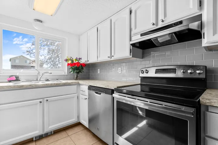 Kitchen with stainless steel appliances, tasteful backsplash, white cabinetry, light tile patterned floors, and a textured ceiling