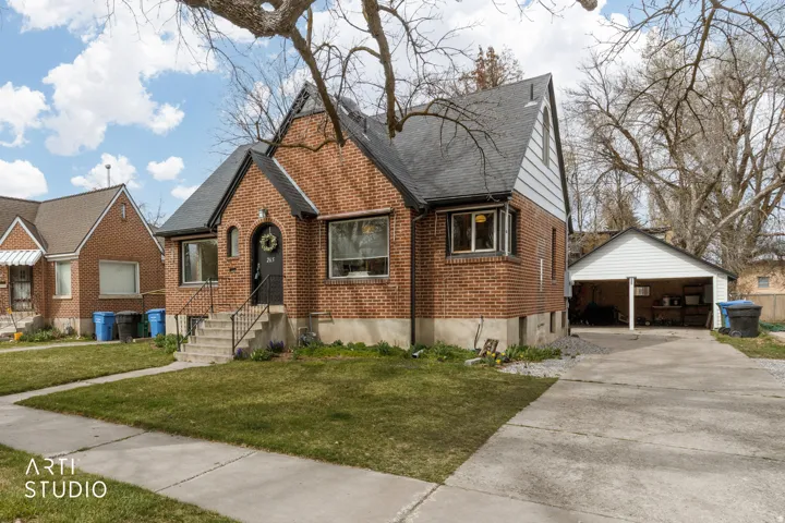 View of front facade with brick siding, an outbuilding, a front yard, a shingled roof, and a garage