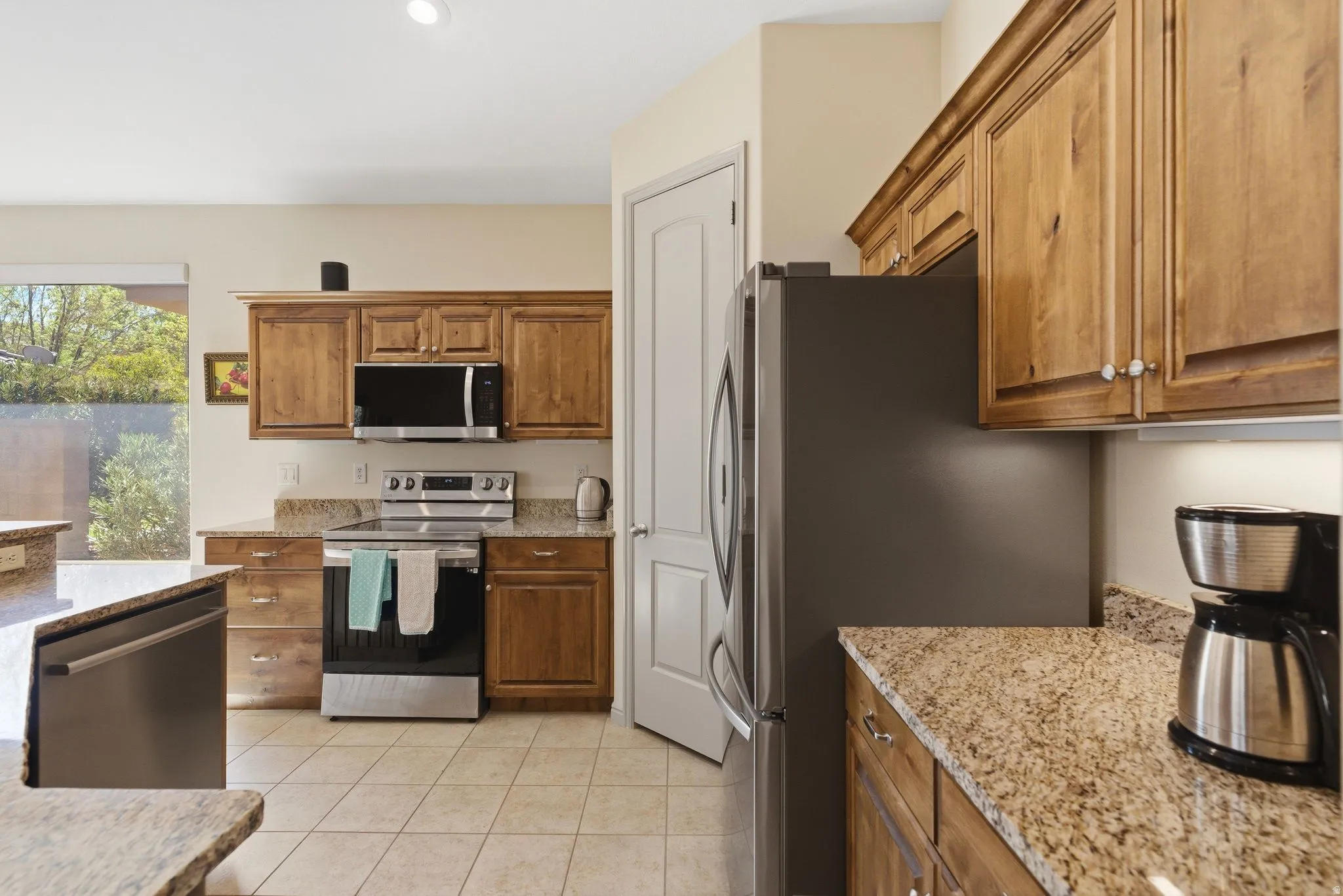 Kitchen featuring stainless steel appliances, light stone counters, wood finish cabinets, and light tile patterned flooring