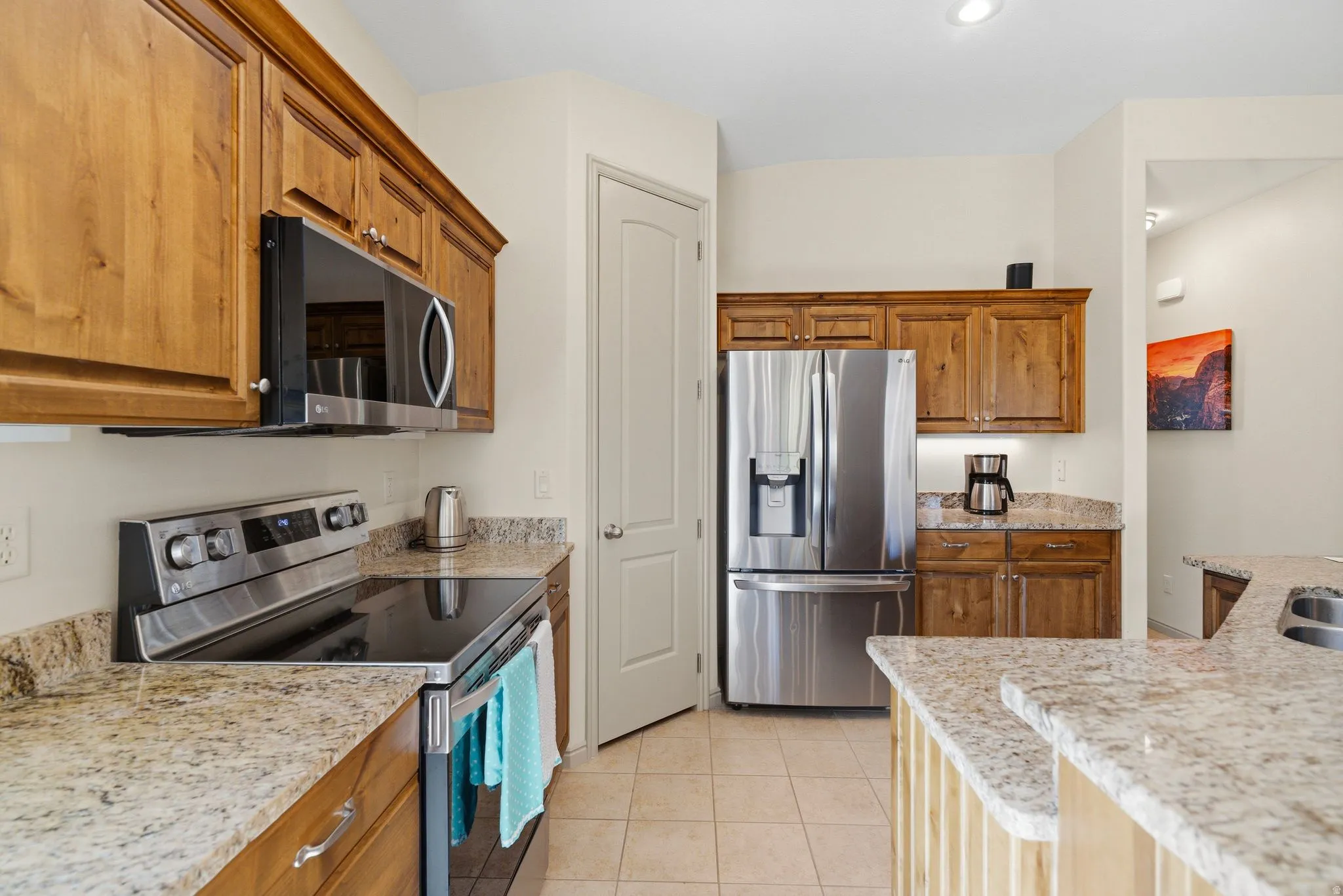 Kitchen featuring stainless steel appliances, light stone counters, wood finish cabinetry, and light tile patterned flooring