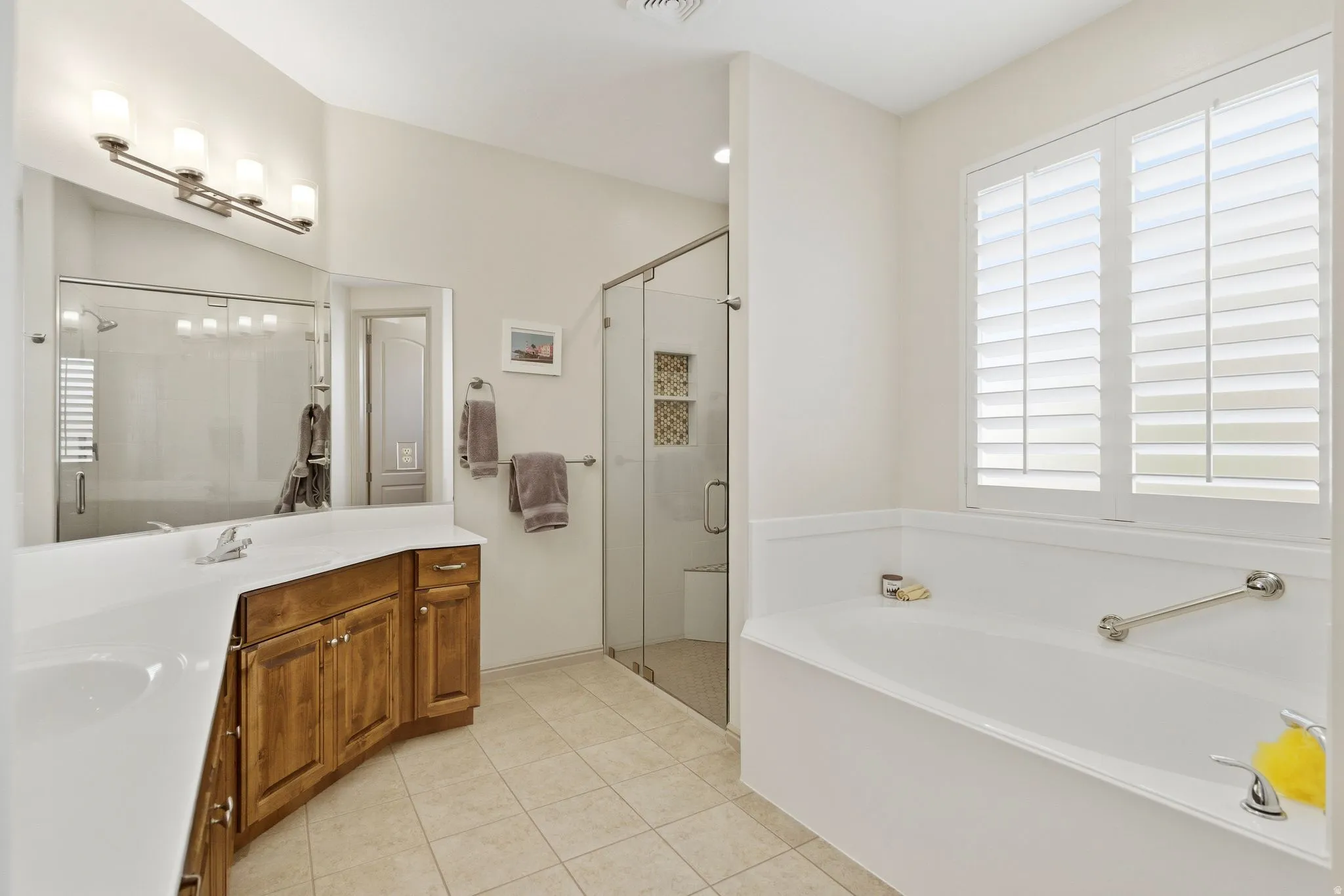 Bathroom featuring double vanity, light tile patterned flooring, a shower stall, and a garden tub