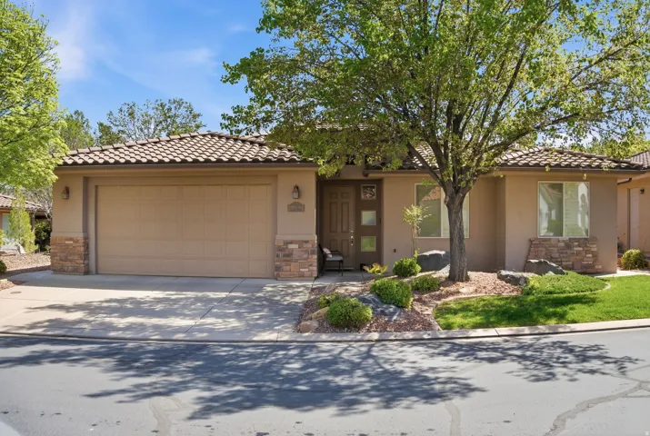 View of front of property with stone siding, a garage, concrete driveway, and stucco siding