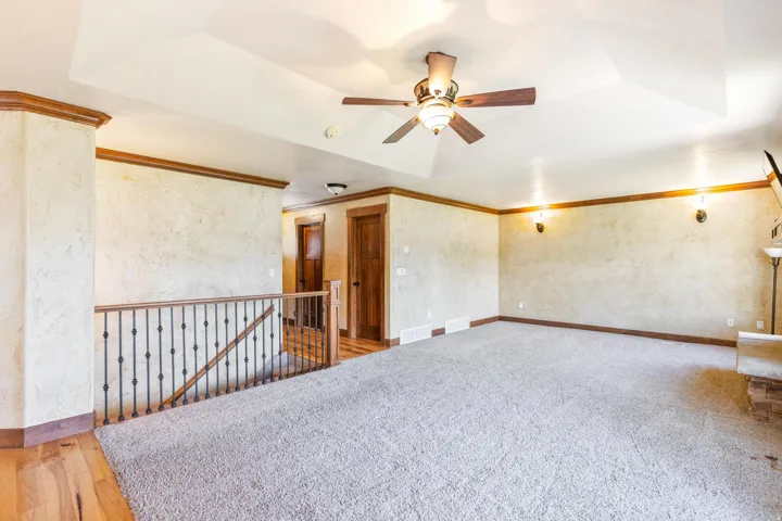 Empty room with a tray ceiling, a ceiling fan, ornamental molding, and light carpet