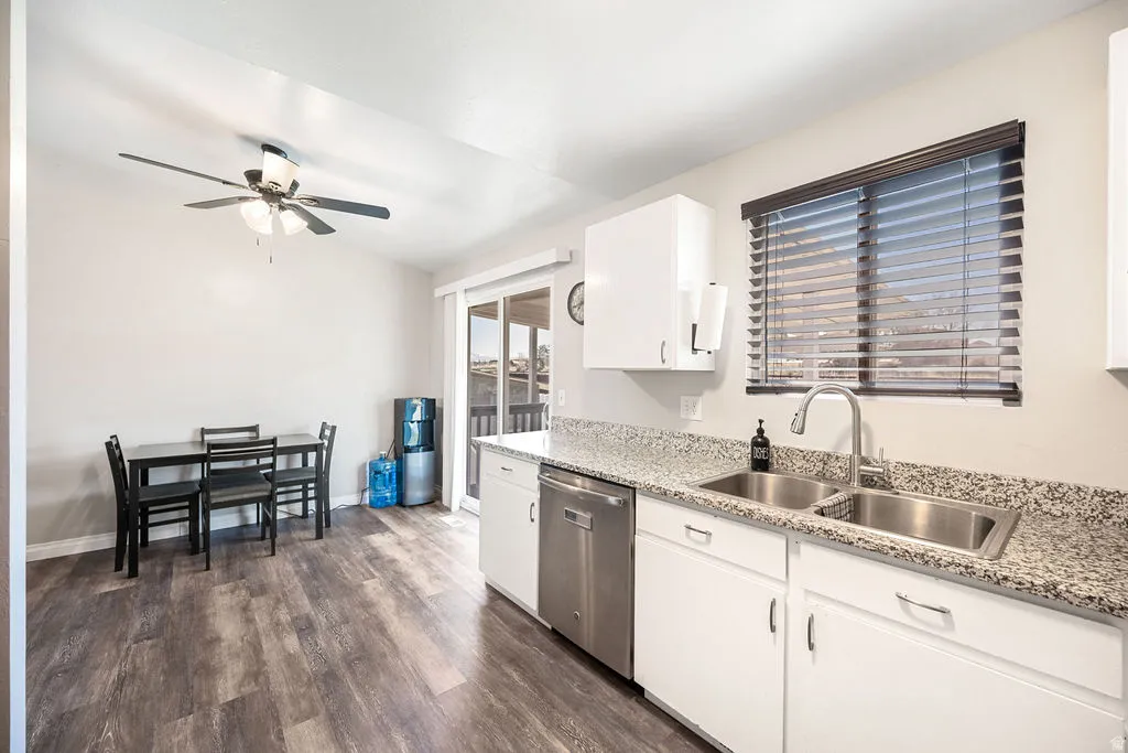 Kitchen with white cabinets, dark wood finished floors, stainless steel dishwasher, ceiling fan, and light stone countertops