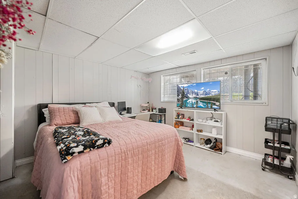 Bedroom with wooden walls, a paneled ceiling, and concrete flooring