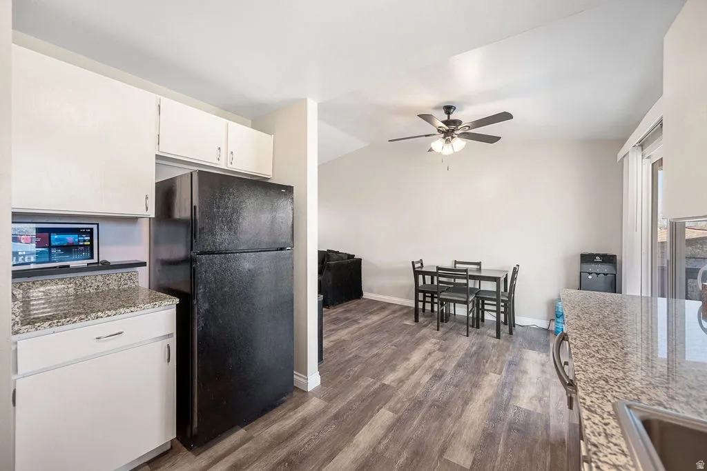 Kitchen with freestanding refrigerator, ceiling fan, dark wood-style floors, vaulted ceiling, and light stone countertops